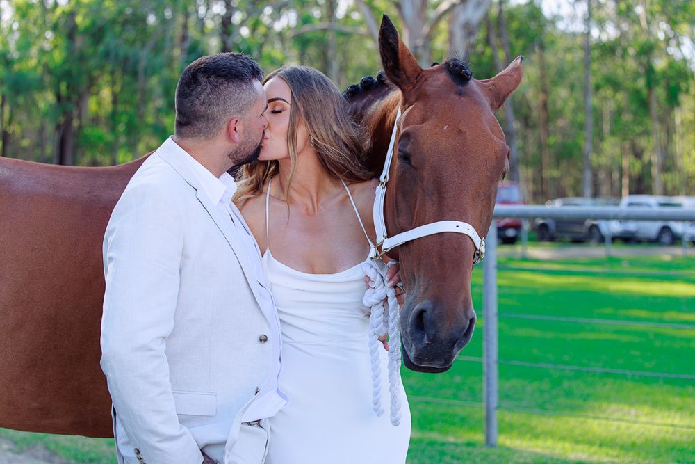 A romantic moment between a couple and their horse in a sunny outdoor setting.