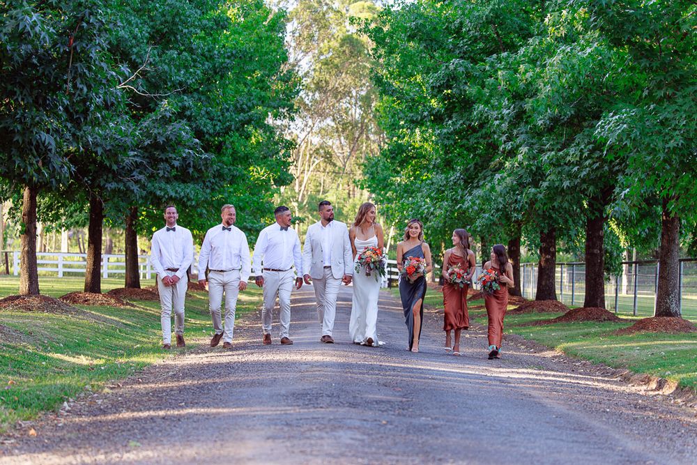Wedding party walking together down a tree-lined path in coordinated attire.