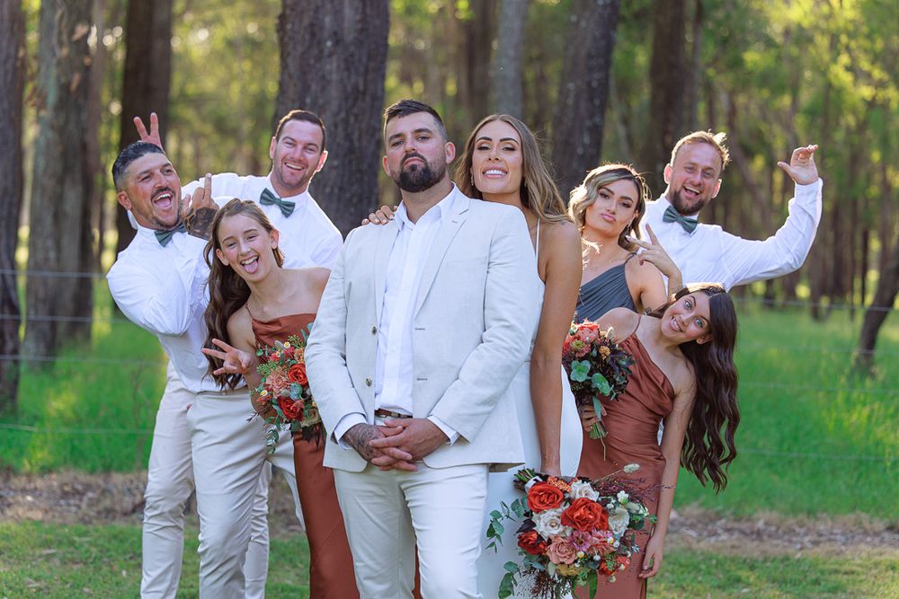 Fun and playful wedding party photo with coordinated poses in a forest setting.