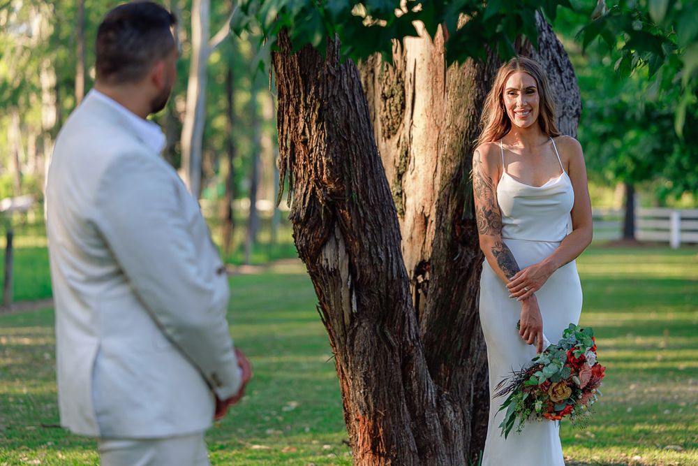 A romantic wedding photo shoot takes place under tall trees in a sunlit forest setting.