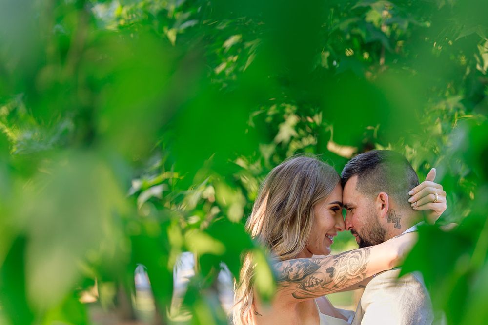 Intimate wedding moment captured through green foliage in a natural outdoor setting.