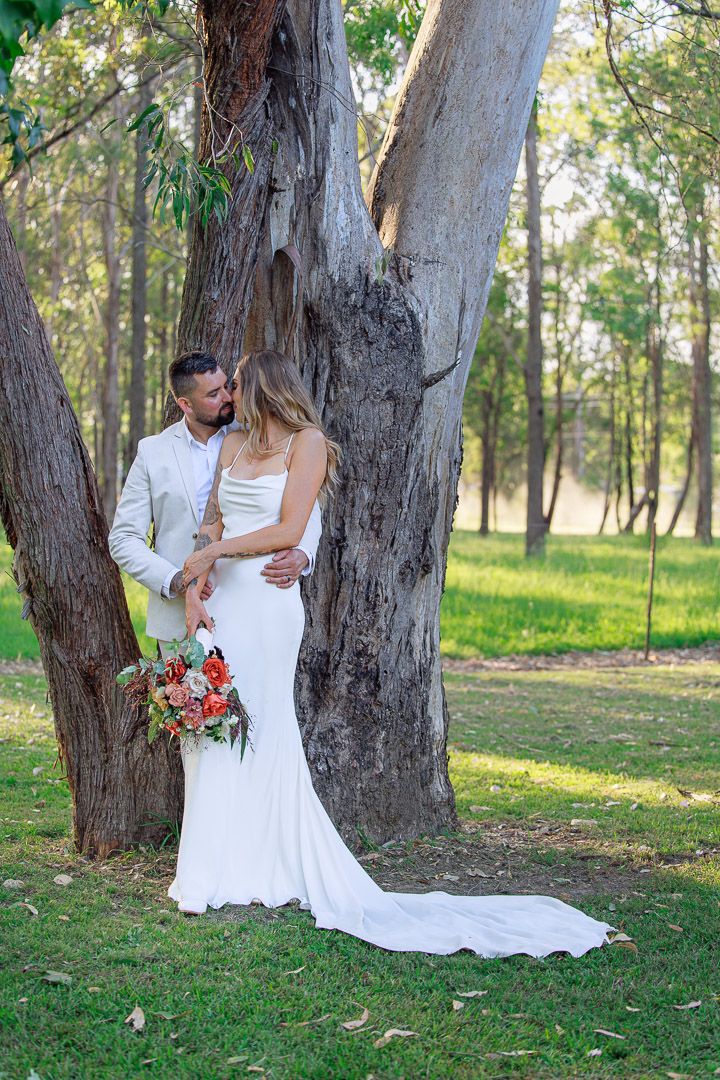 Romantic wedding portraits captured against rustic tree trunks in a sunlit forest.