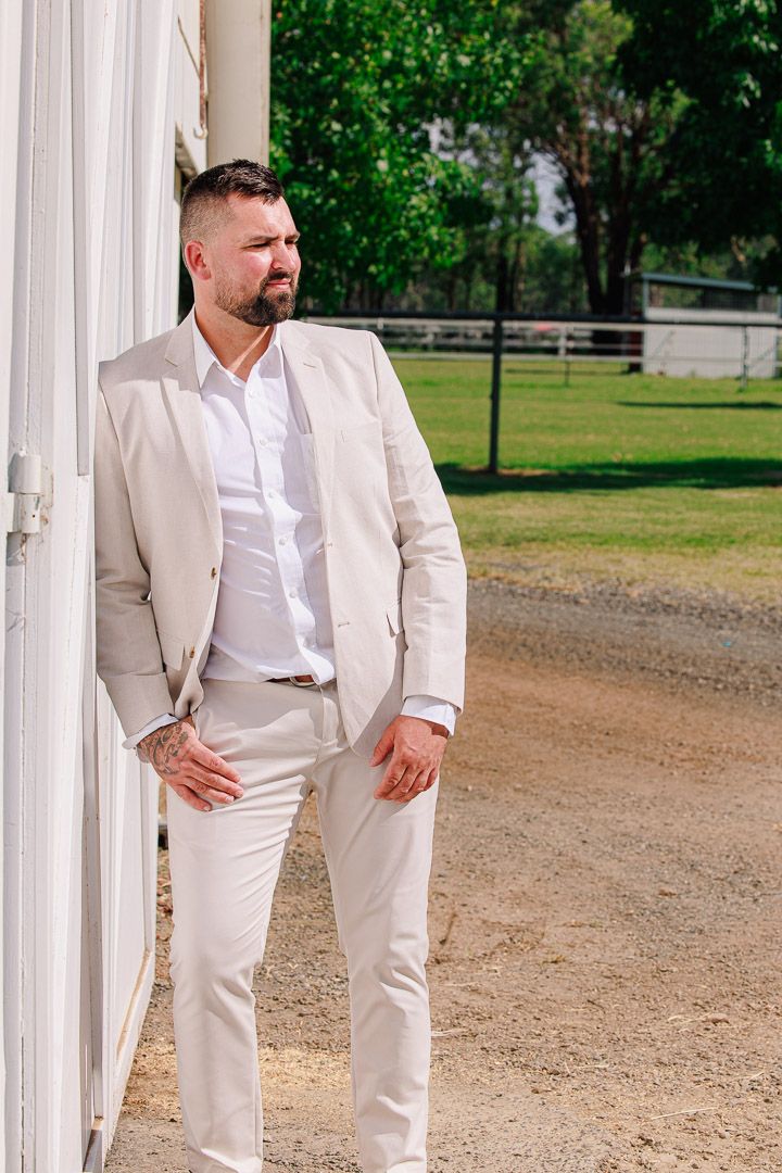 Groomsmen in cream suits and white shirts pose casually outside rustic barn.
