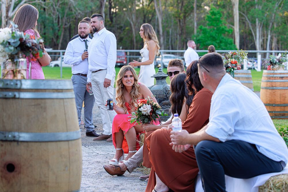 Outdoor wedding reception with guests seated at rustic tables near wine barrels.