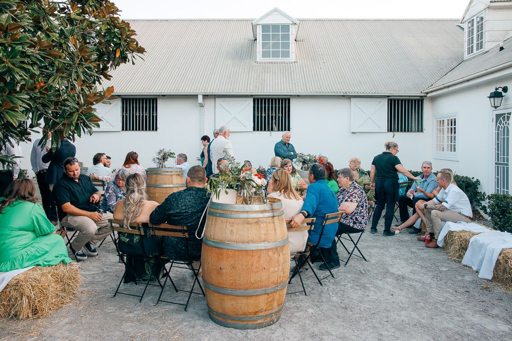 Wedding reception setup with hay bales and wine barrels outside a white building.