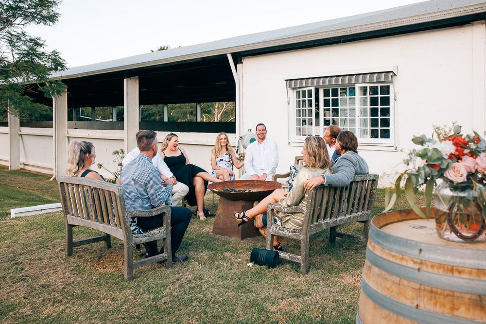 Rustic outdoor wedding reception with wooden benches and wine barrel decor.