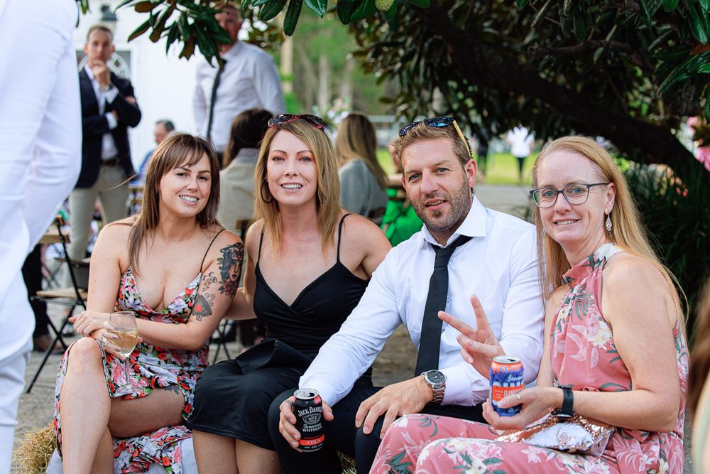 Casual outdoor wedding reception with guests enjoying conversation under tree canopy.