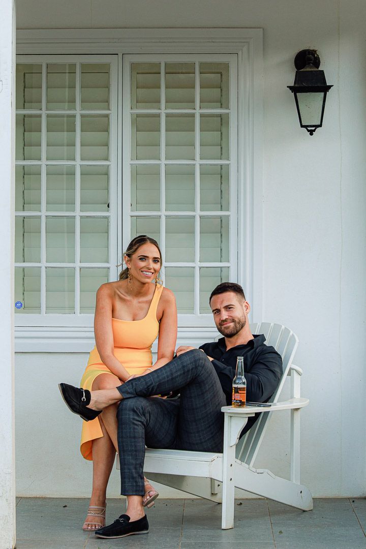 Couple relaxes on white porch chairs during casual outdoor photoshoot.