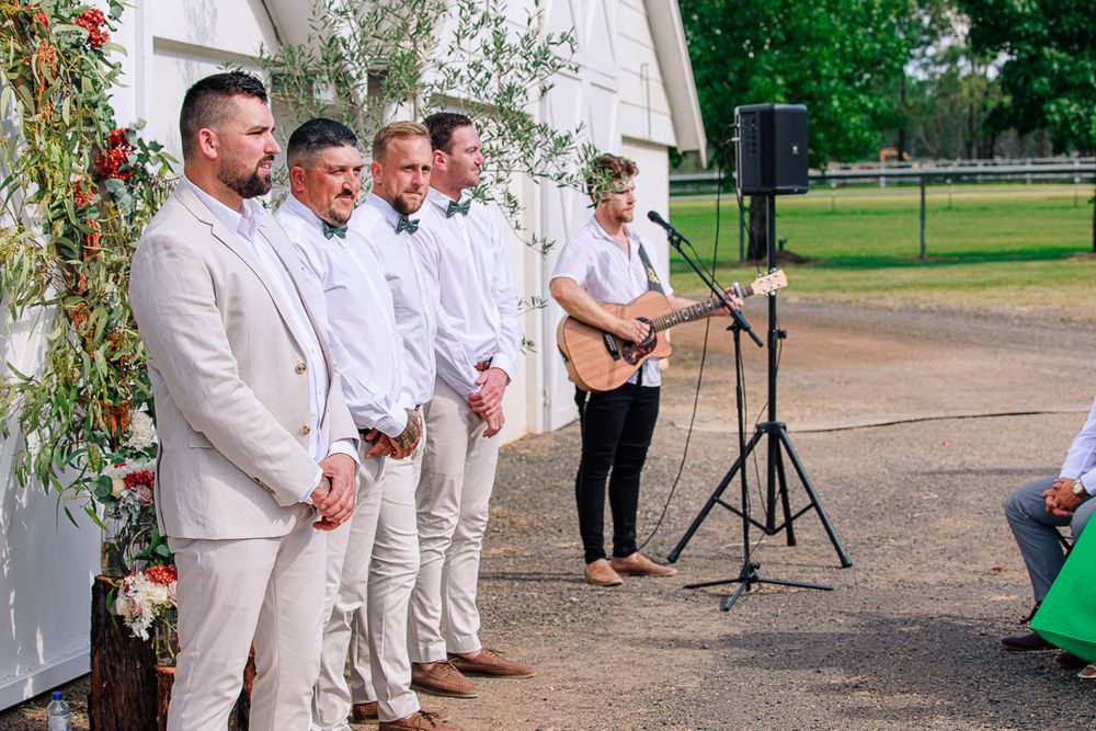 Wedding party in white attire stands together during an outdoor ceremony celebration.