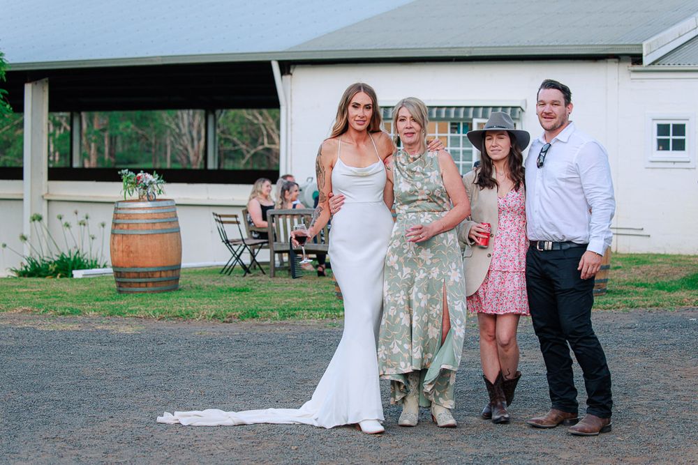 Wedding party poses casually outdoors near rustic barn setting.