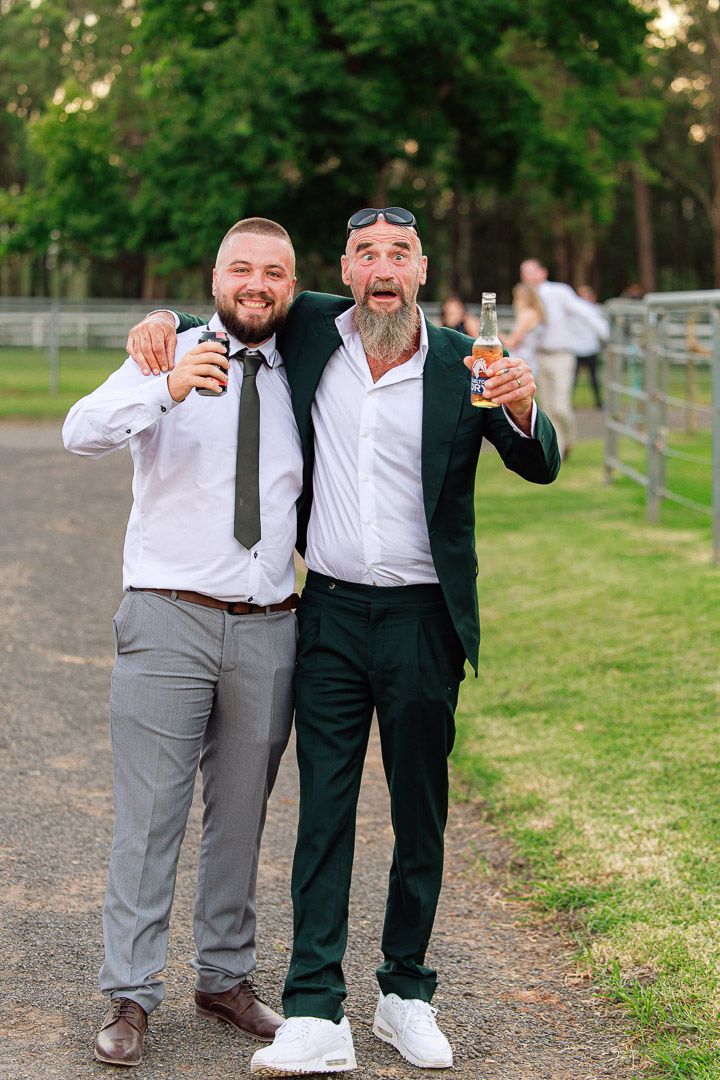 Friends in formal attire share drinks and laughs outdoors.