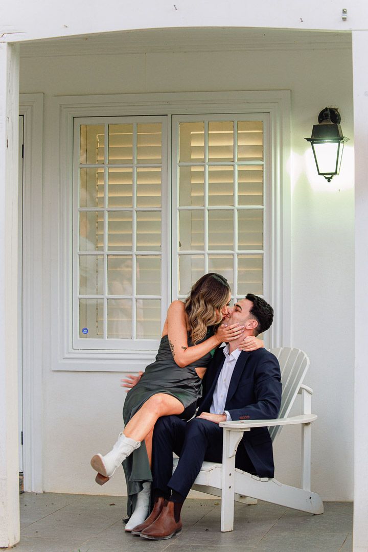 Romantic couple shares intimate moment on white porch bench.