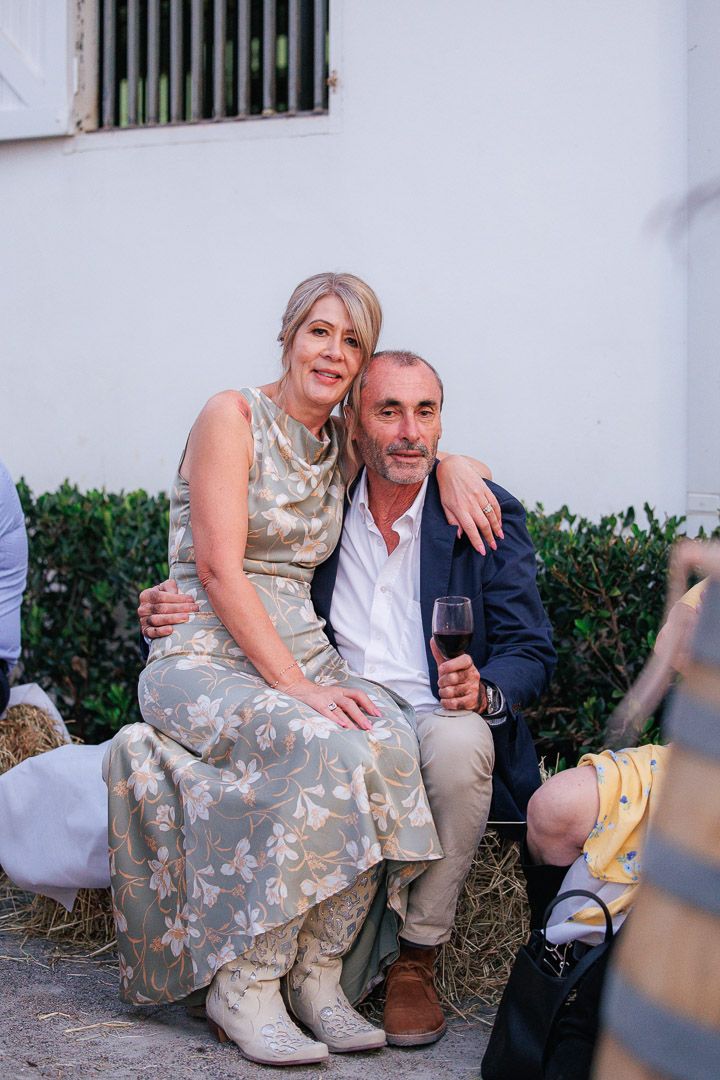 A couple sits casually on stone steps at an outdoor event, sharing drinks and laughter in an intimate moment.