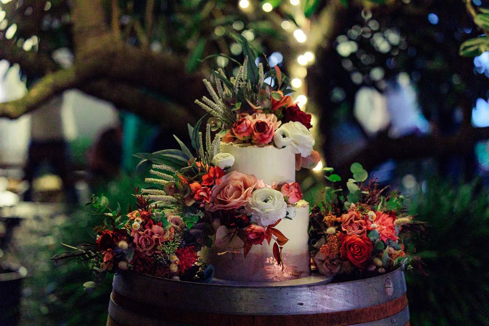 Elegant floral arrangements with red and pink blooms decorate a rustic wooden barrel at an outdoor venue.