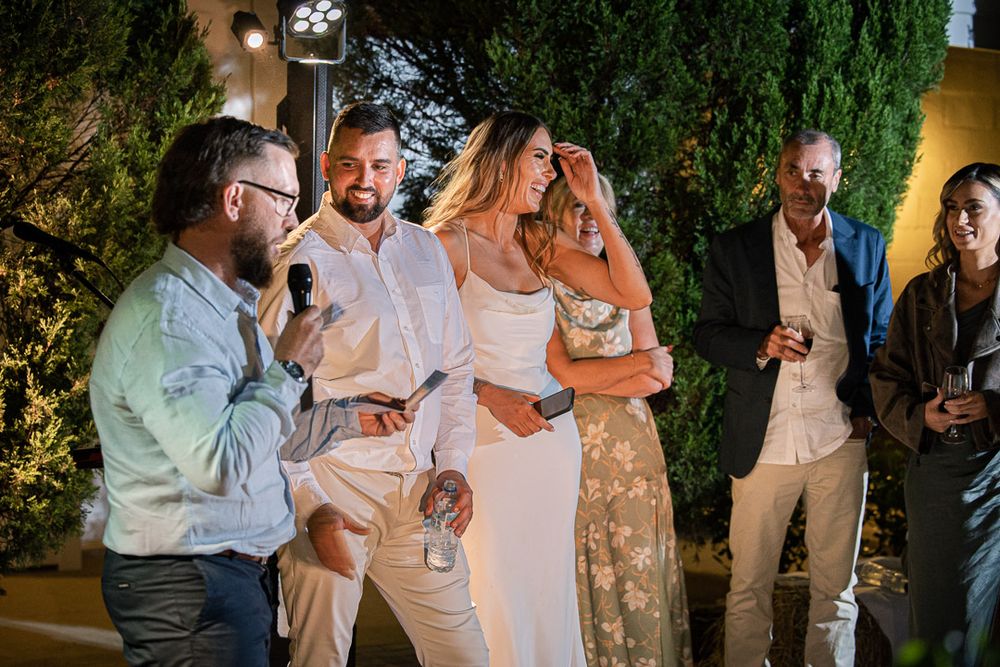 Wedding guests gather outdoors in the evening, mingling and socializing under garden lighting.