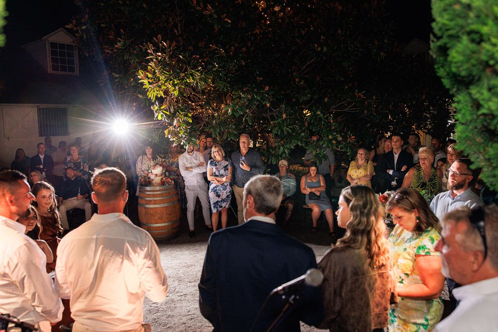 Evening celebration with guests mingling under outdoor lighting and garden foliage.