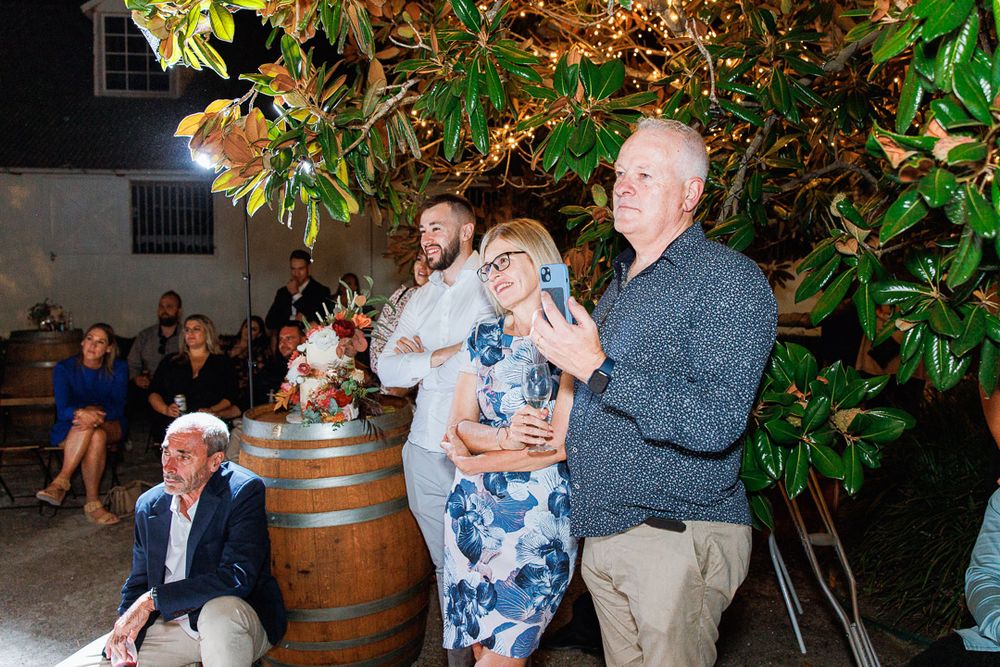 Party guests socializing and dancing at an outdoor evening celebration near wooden barrels.