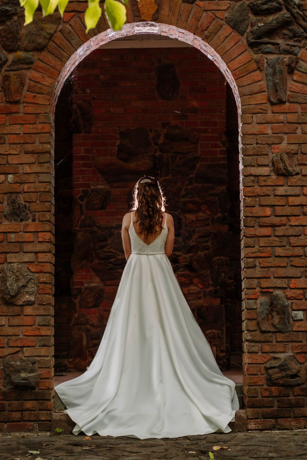 Backlit photo of a bride standing under a wedding arch, glowing in natural light during a romantic outdoor portrait session.