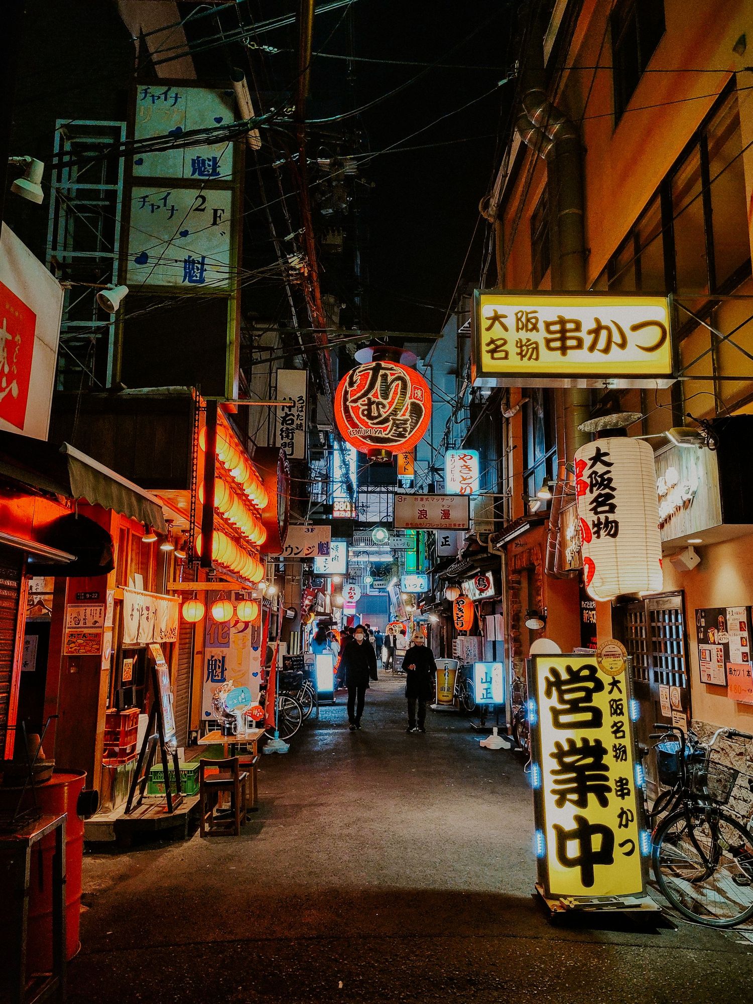 a narrow side street that is very full of lights and store signs in Osaka Japan