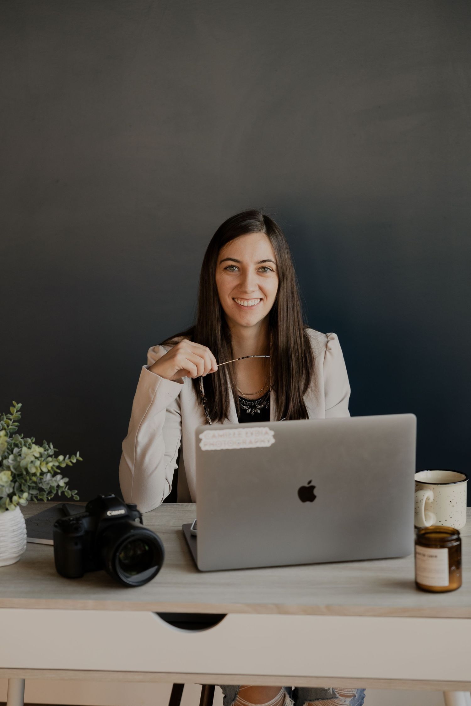 Creative professional working at desk with laptop and camera in modern office setting.