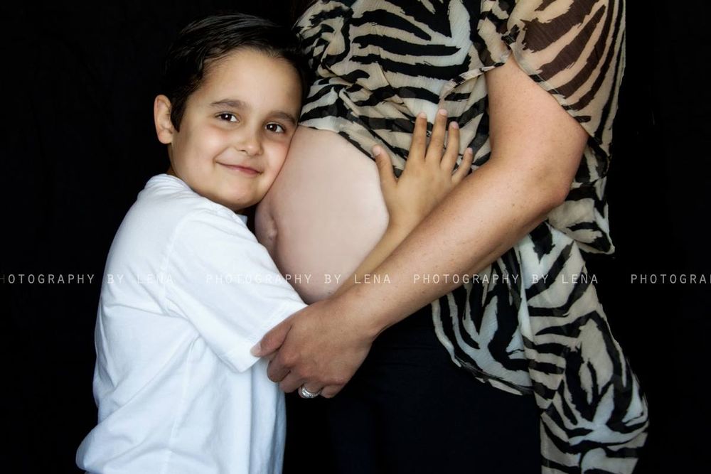 Maternity photo featuring child hugging pregnant belly against zebra print background.