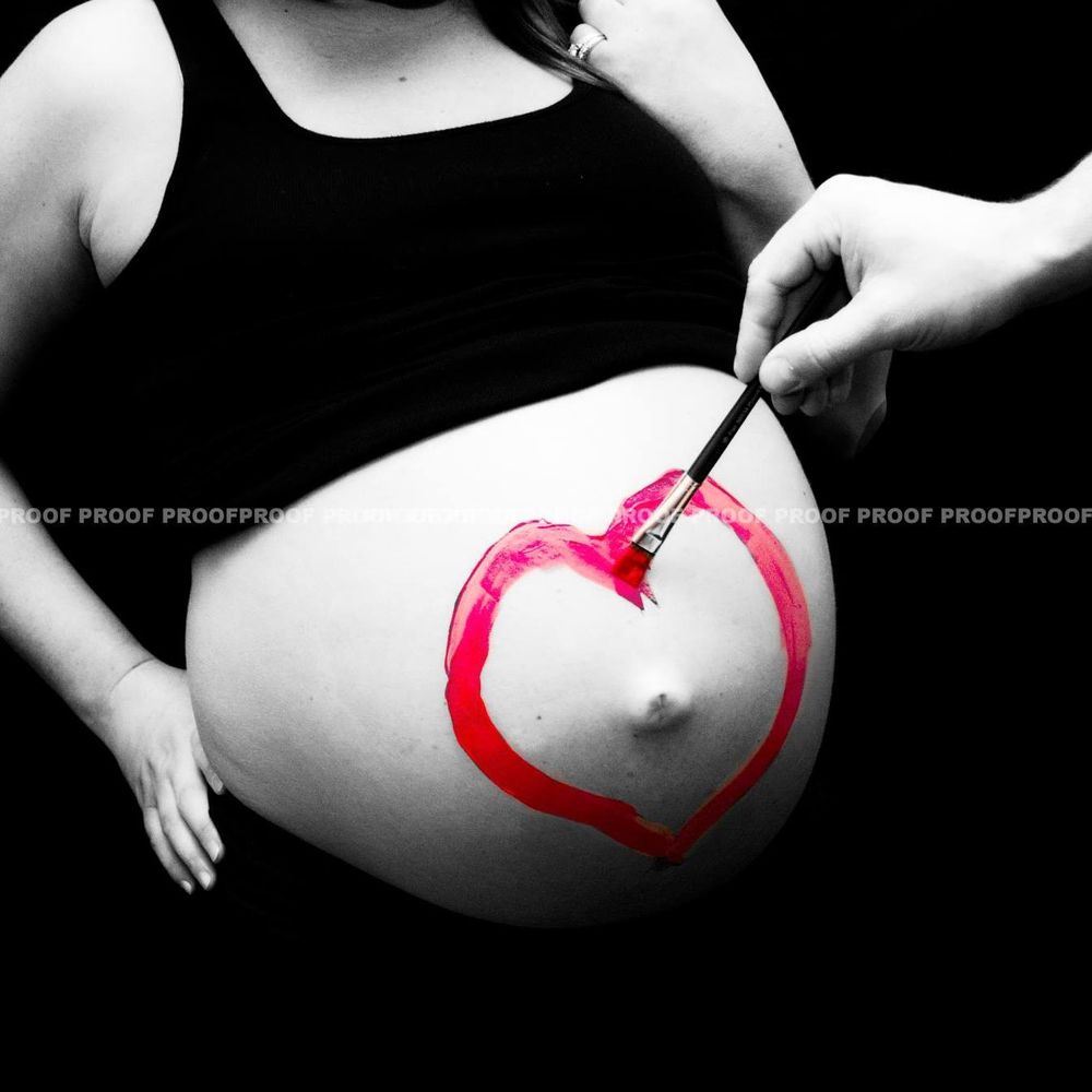 Creative maternity photo with red heart drawn on pregnant belly in black and white.