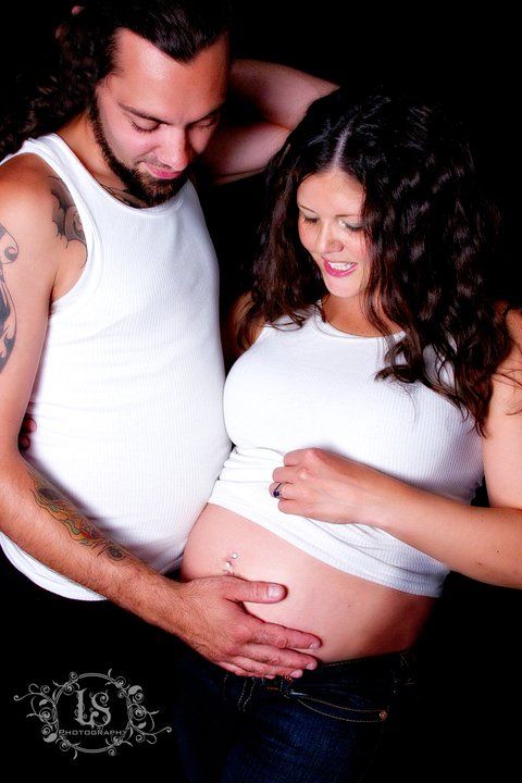 Intimate maternity photos showing couple in white tops against dark background.