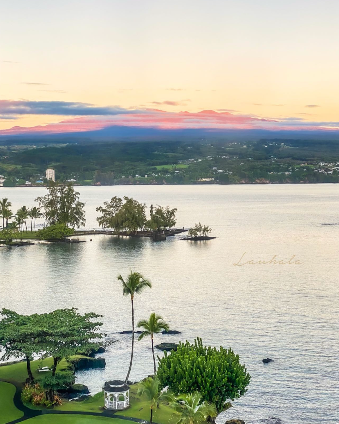 Aerial view of a tropical island cove with palm trees and buildings at sunset in Hawaii.