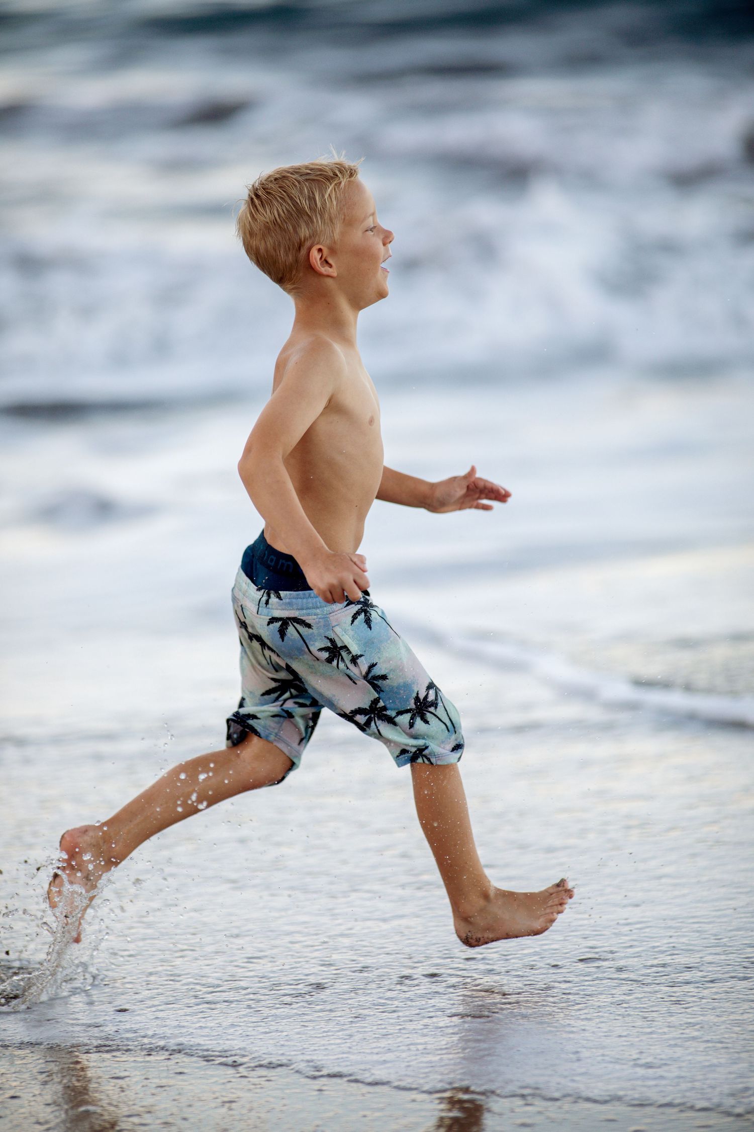 Boy running alongside the beach with a smile on his face and making splashes with his feet.