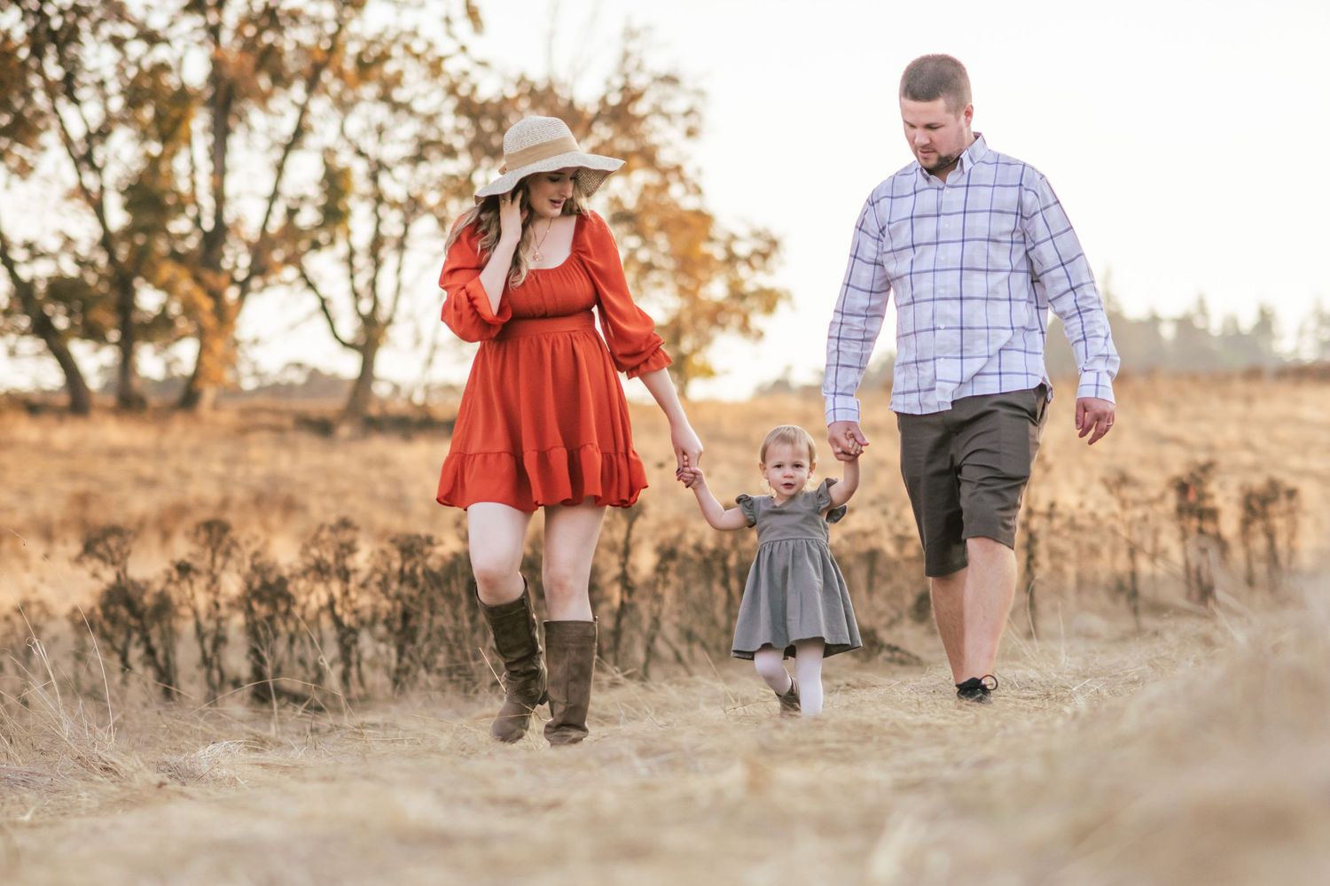 Family of 3 walking in field holding hands. mom and dad looking at daughter.
