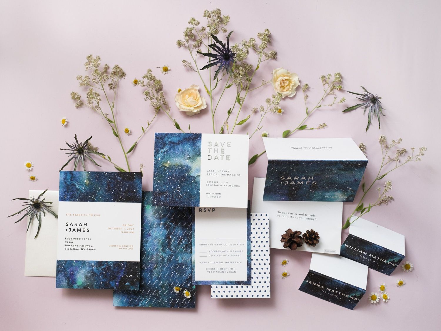 Wedding invitation suite with galaxy-inspired design, black spiders, and delicate white flowers arranged on pink background.