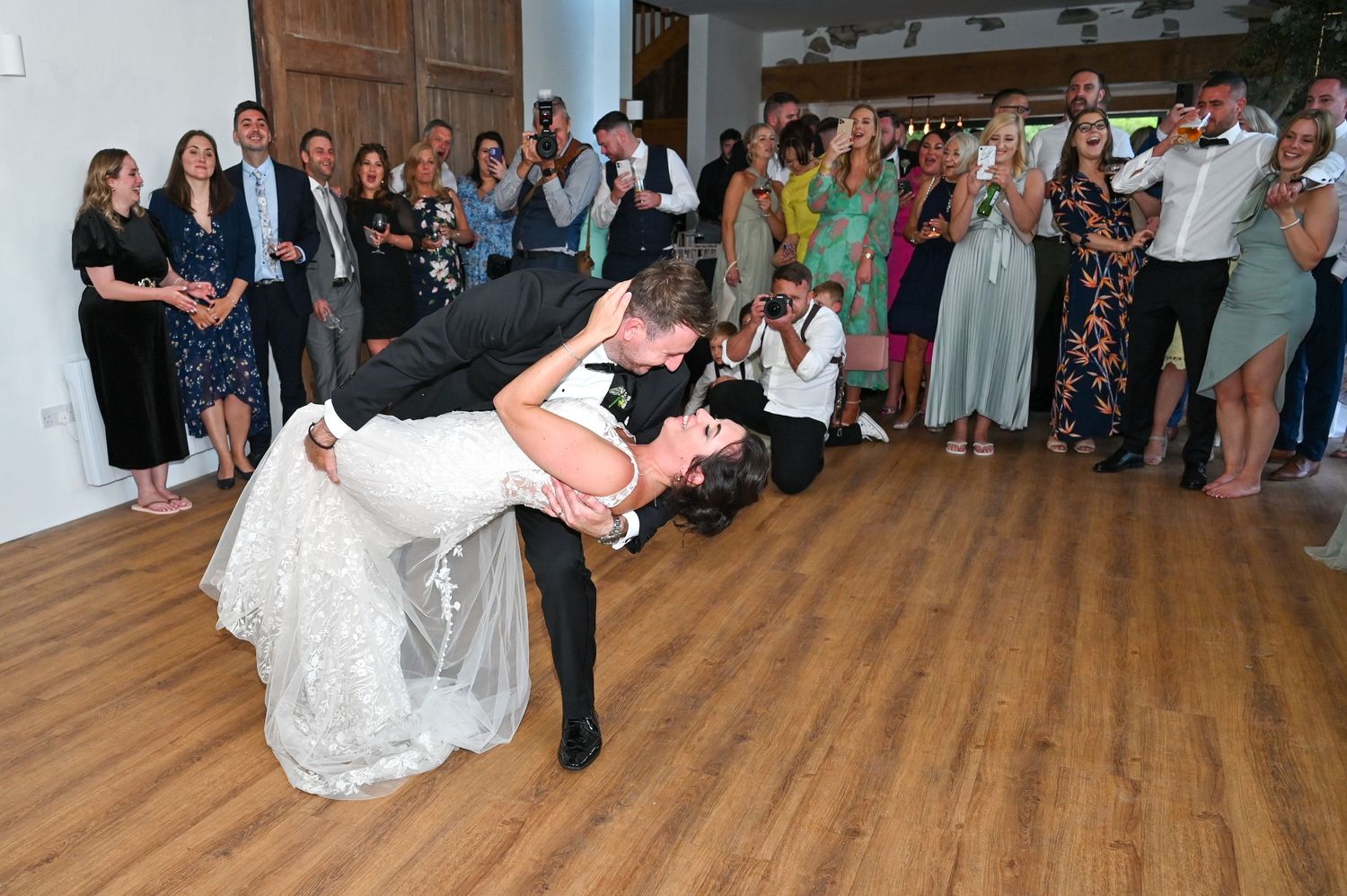 A romantic dance dip at a wedding reception with guests watching on the wooden dance floor.