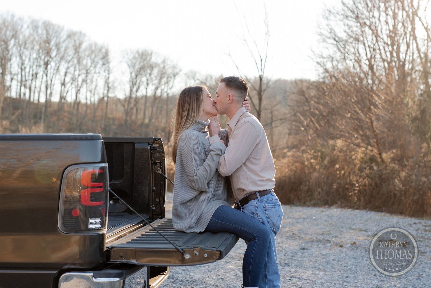 Couple sharing romantic moment on tailgate of pickup truck at sunset.