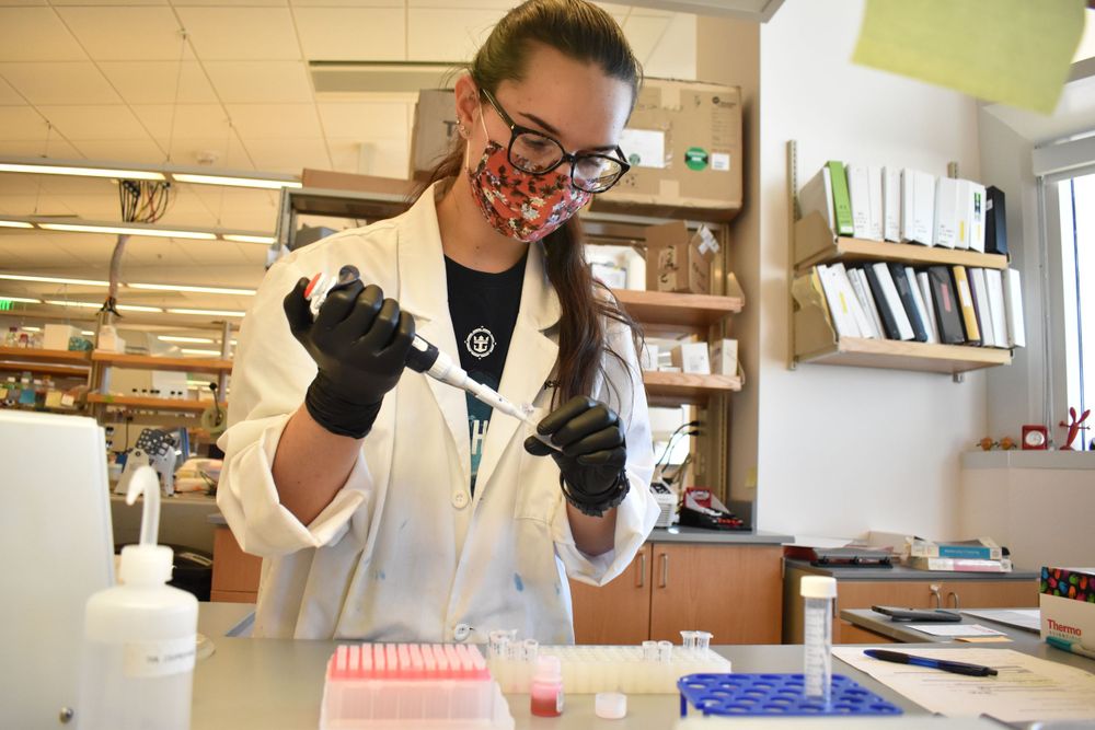 Researcher in lab coat and protective gear conducts experiments with scientific equipment.