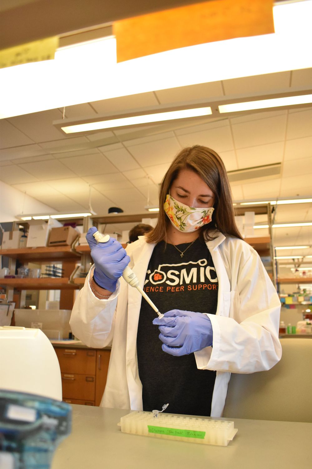 Scientist wearing mask and gloves performs laboratory work with test tubes and equipment in research setting.