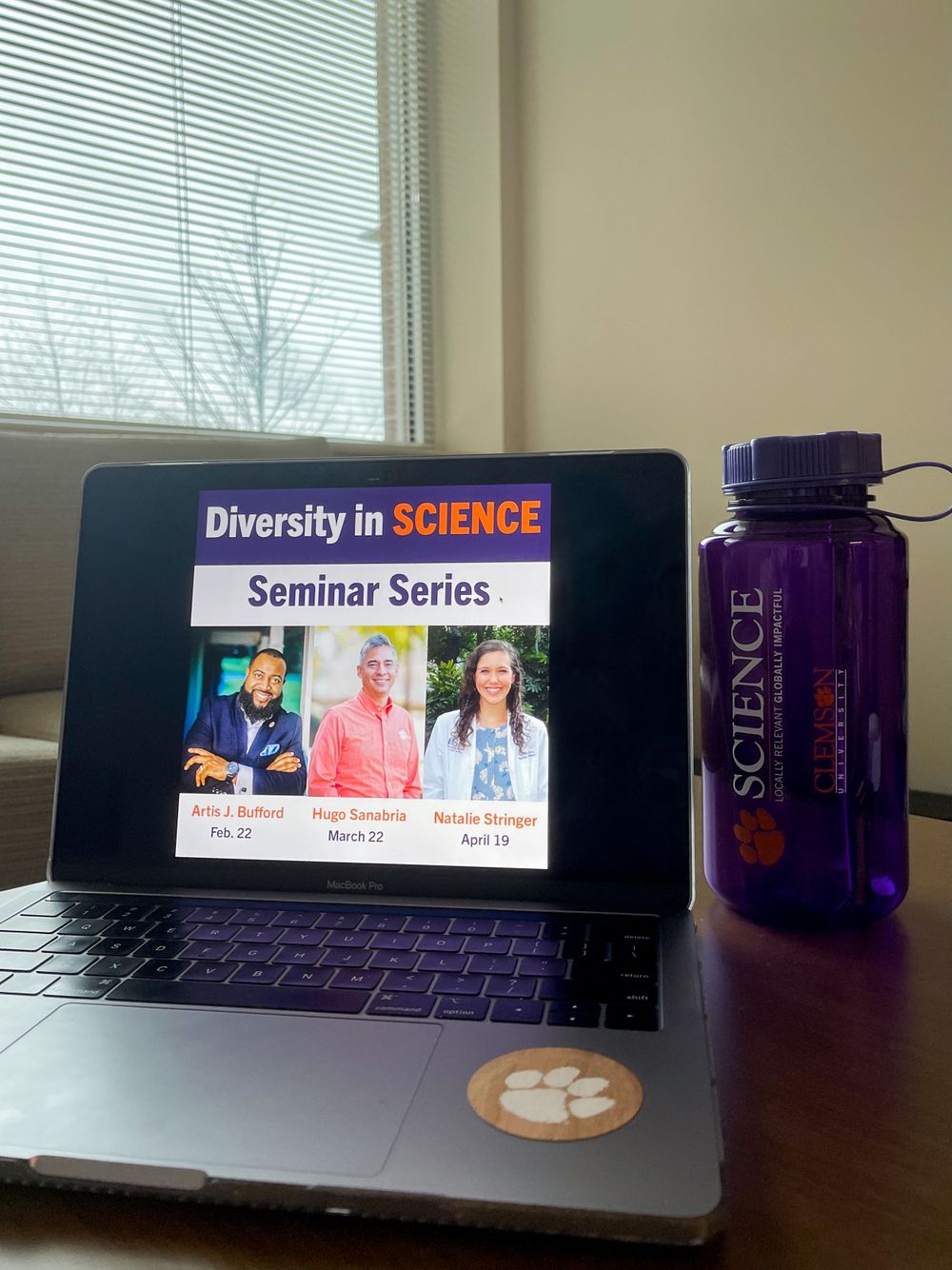Laptop displaying seminar series information with purple water bottle and Clemson sticker.