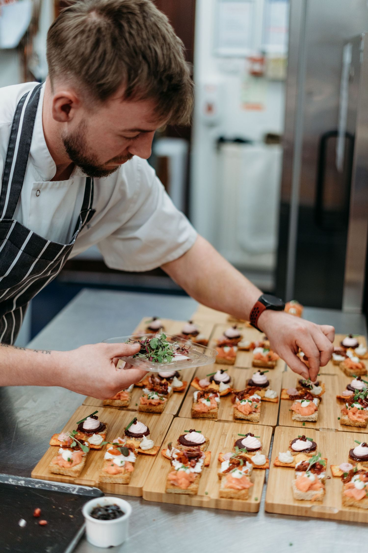 Chef in striped apron carefully plating delicate appetizers on wooden serving boards.
