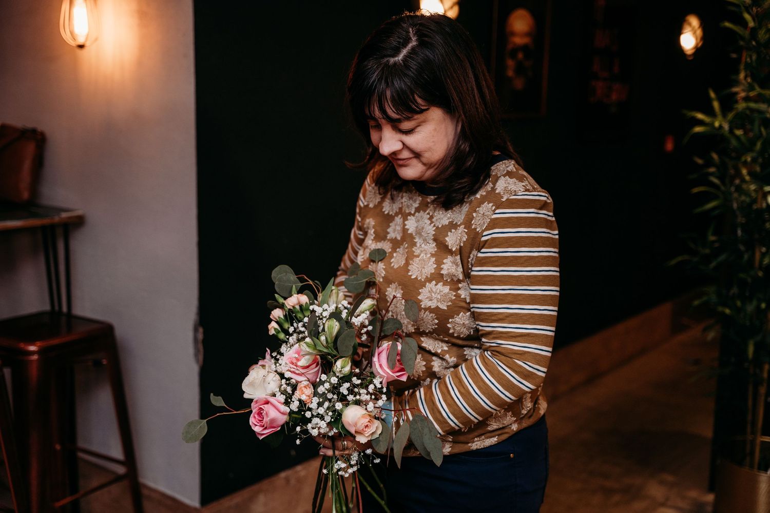 Person holding fresh floral arrangement in indoor setting with warm lighting.