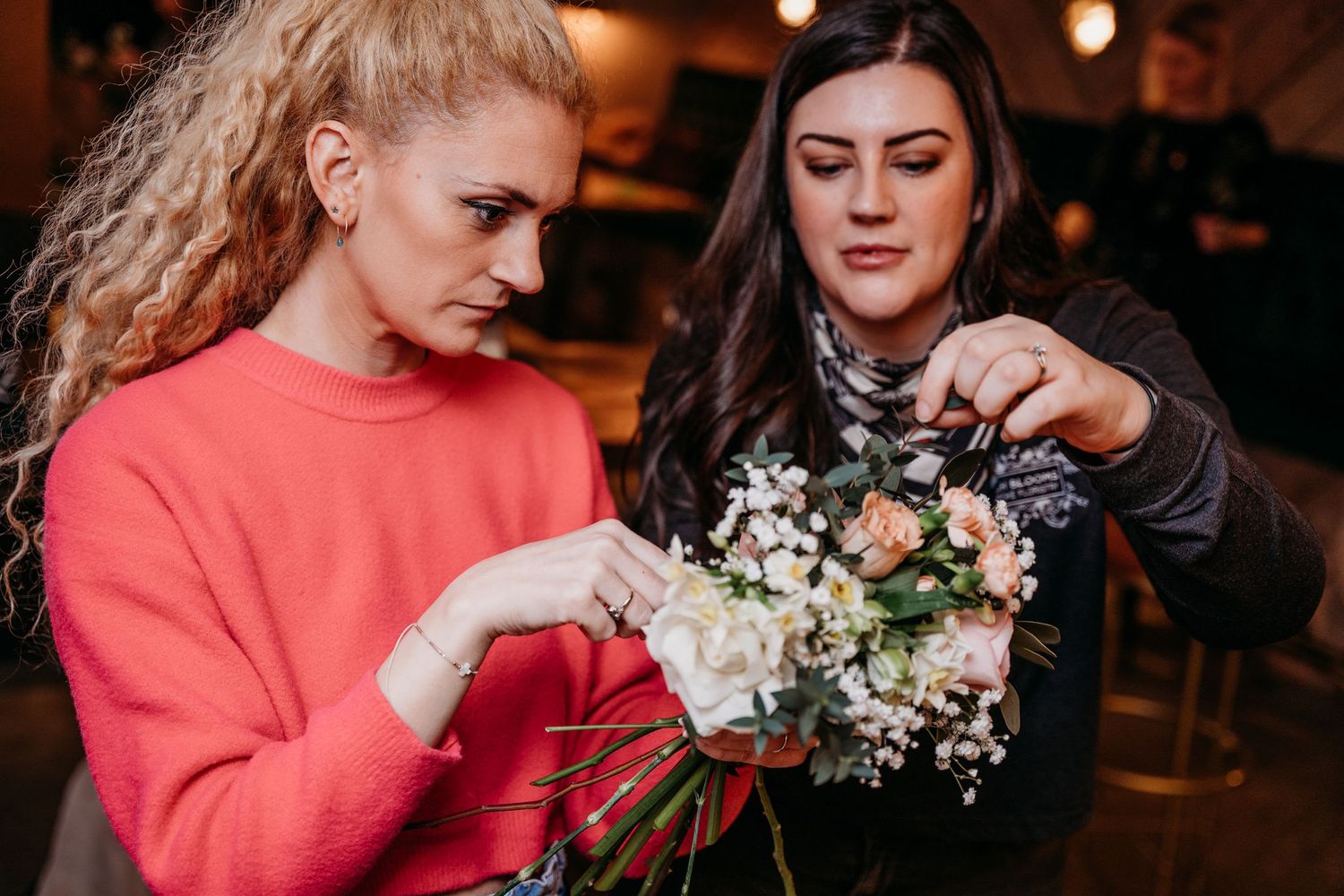 Two people collaborating on floral arrangement in indoor workshop setting.