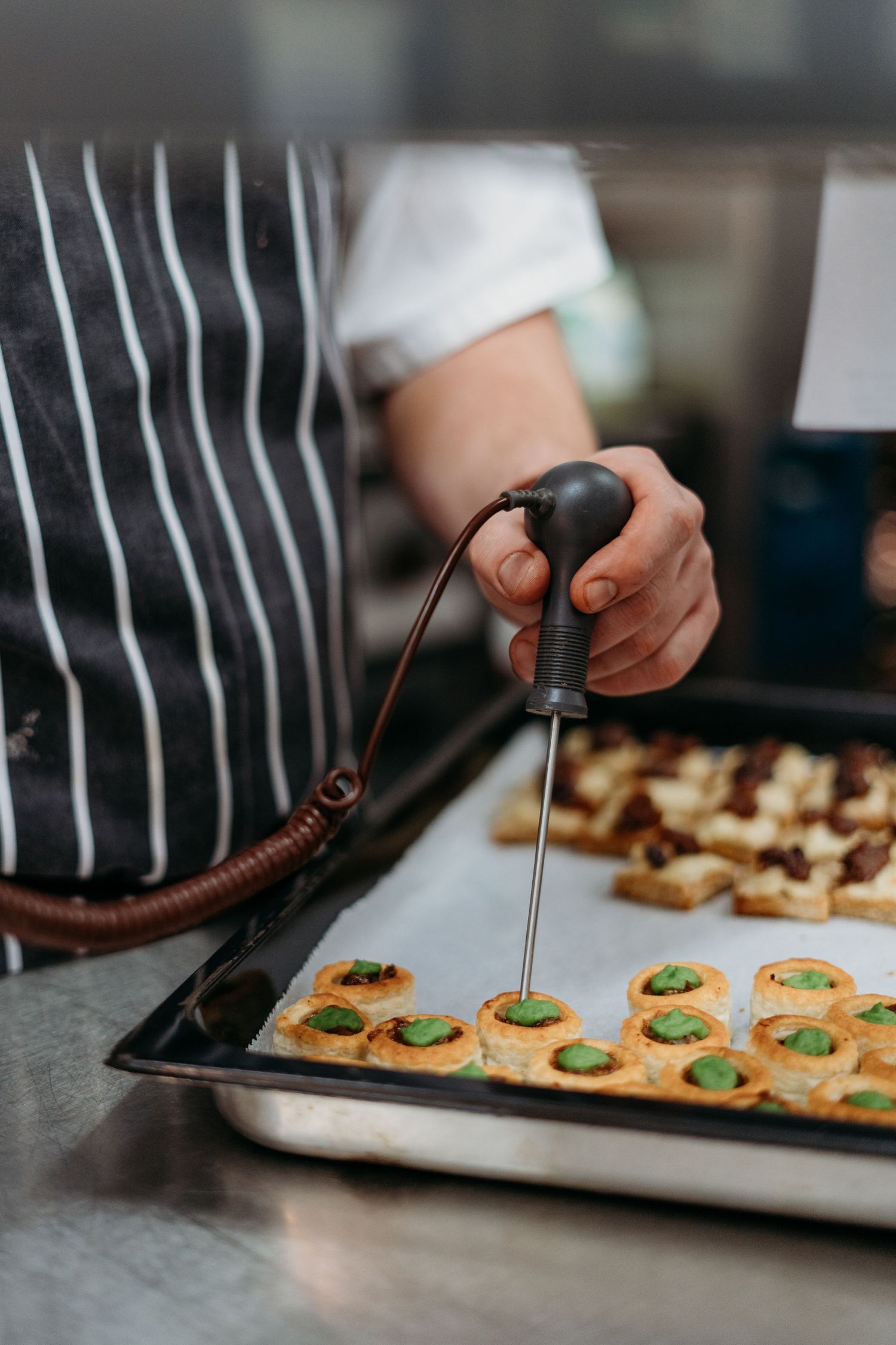 Close-up of chef piping garnish onto appetizers on baking sheet.