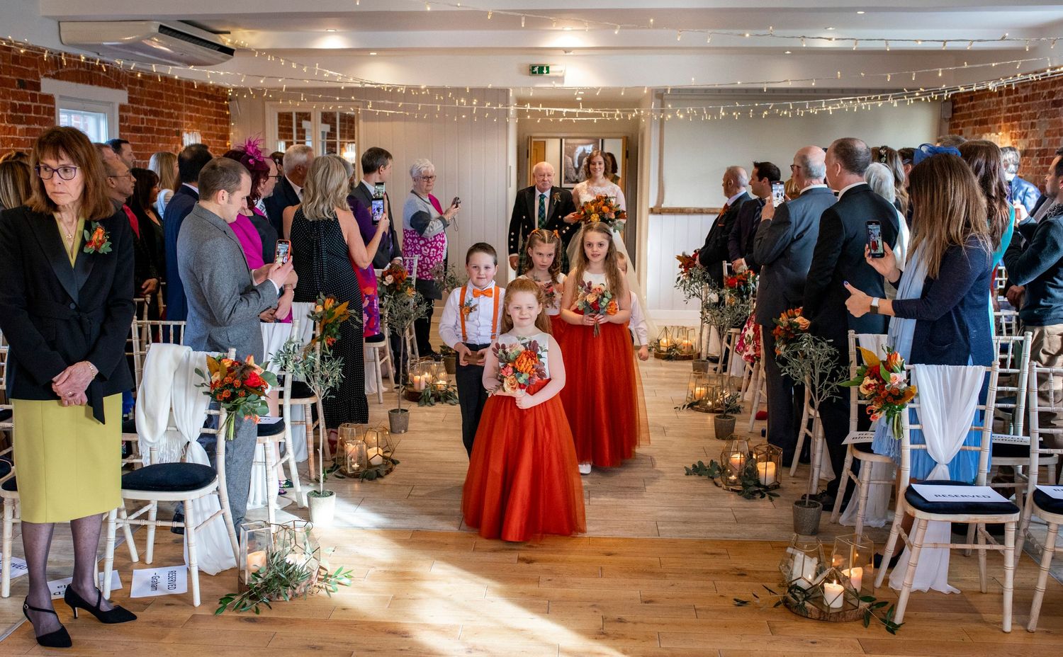 Wedding ceremony processional in a rustic venue with exposed brick walls and string lights.