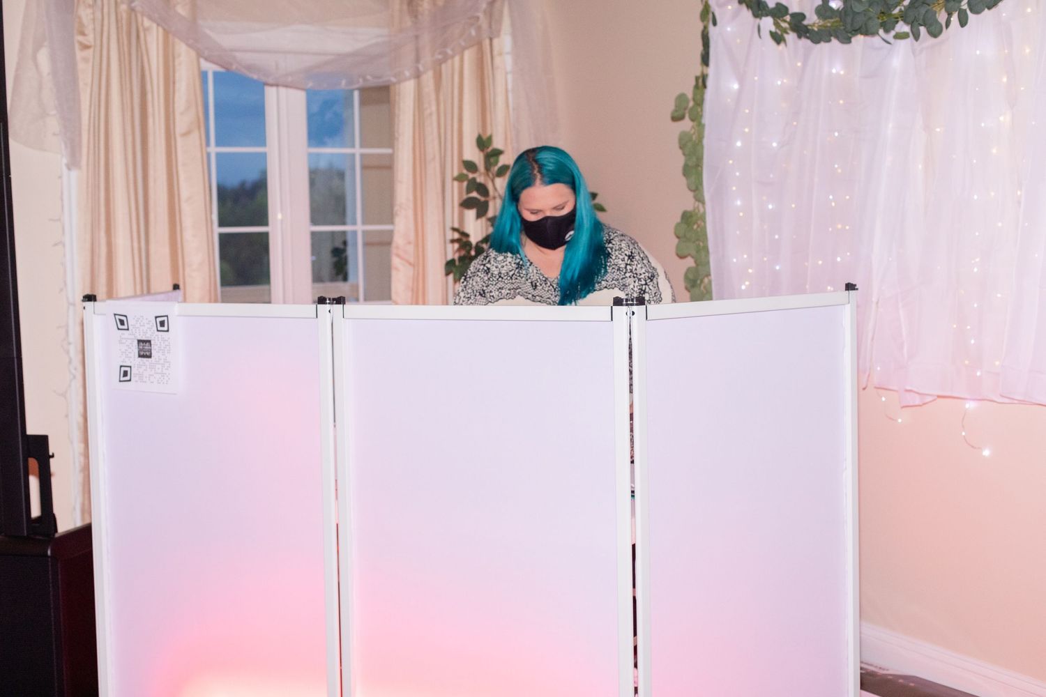 White fabric backdrop with greenery decorations and lighting for wedding ceremony or photo area.