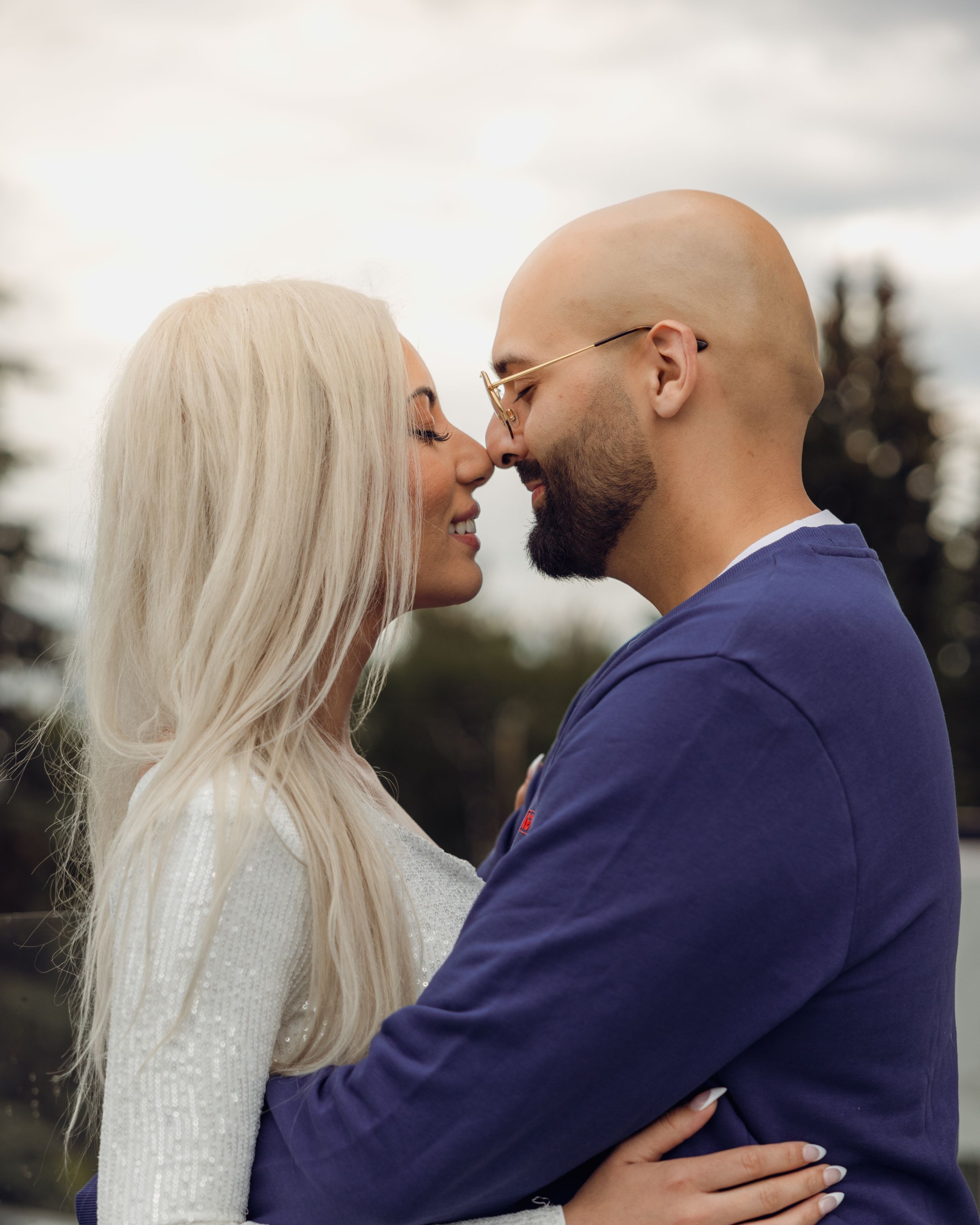 A romantic outdoor portrait of a couple in intimate embrace against a cloudy sky.