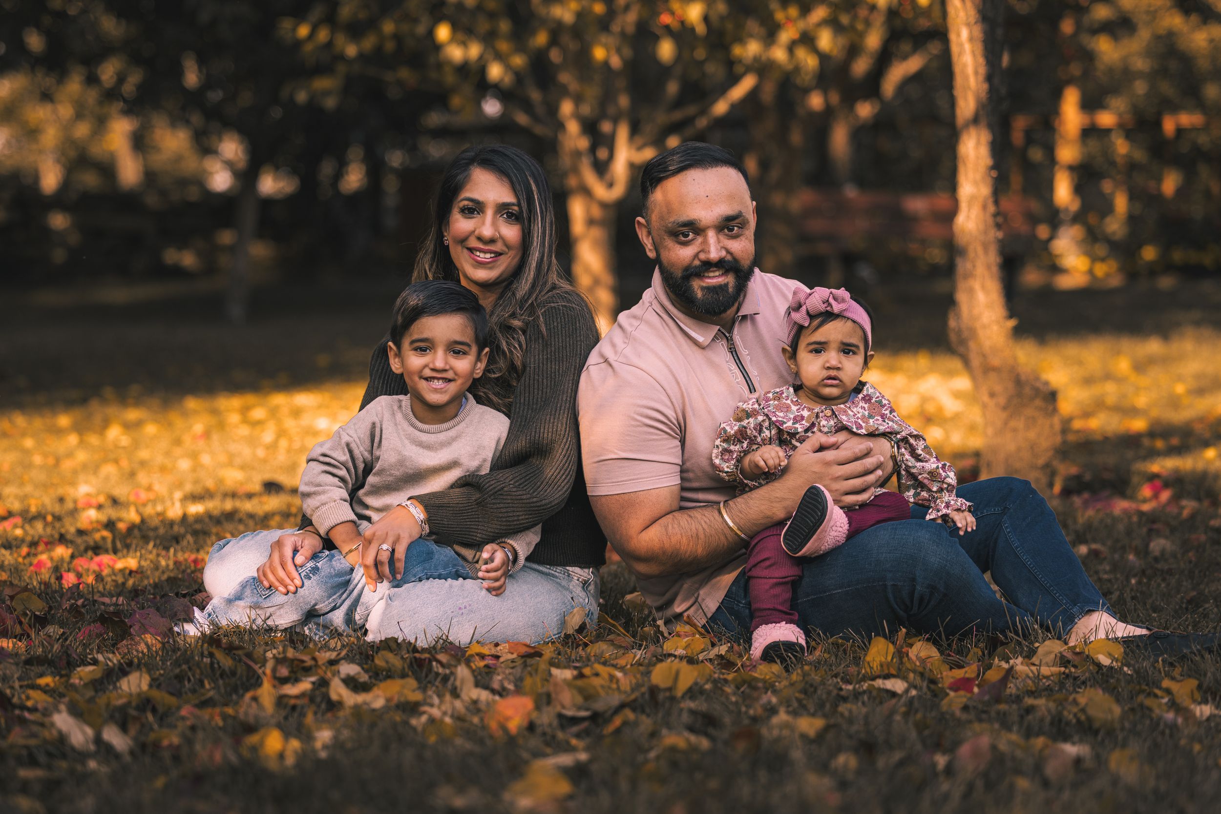Family sitting together on fallen autumn leaves in a park setting.