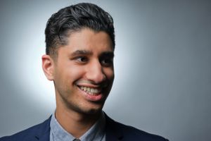 Professional headshot of person in navy suit against grey background.