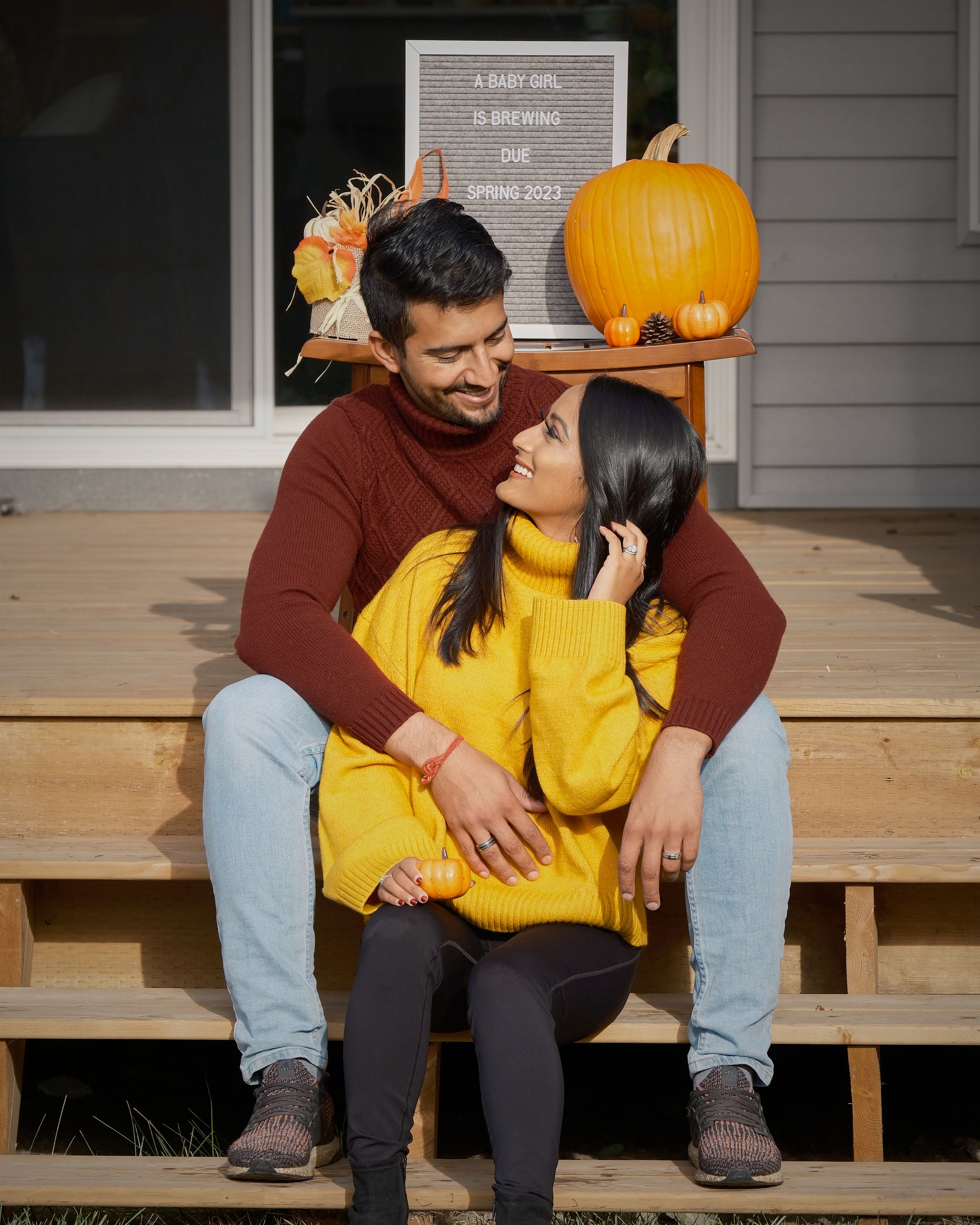 Couple on porch steps with pumpkin decor sharing intimate moment.