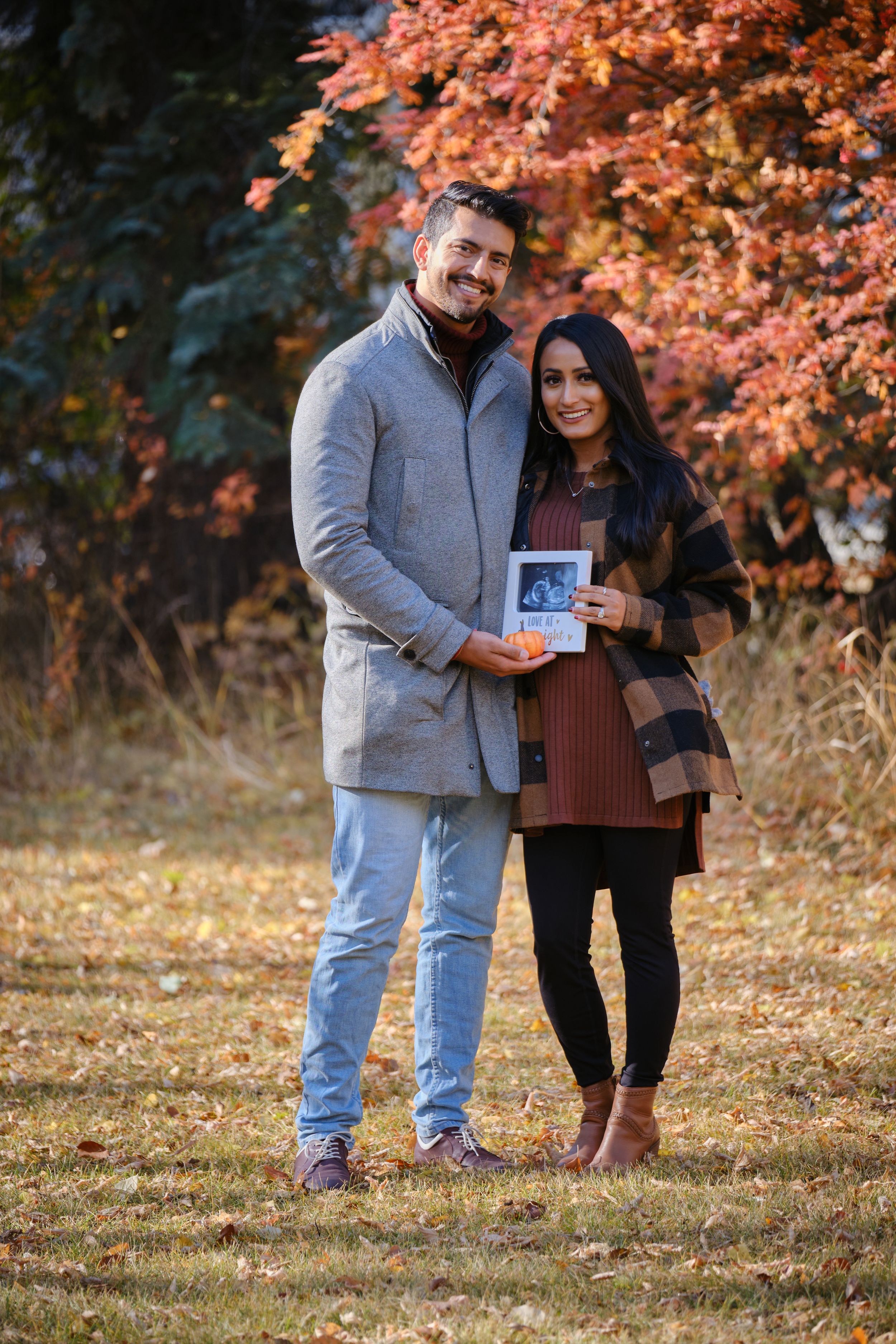 Couple holding ultrasound photo in autumn setting with orange foliage.