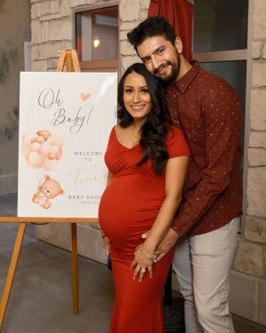 Baby shower celebration scene with couple posing by 'Oh Baby' sign and decorative easel.