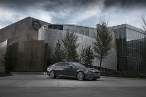Modern grey luxury car parked in front of contemporary glass and concrete building.