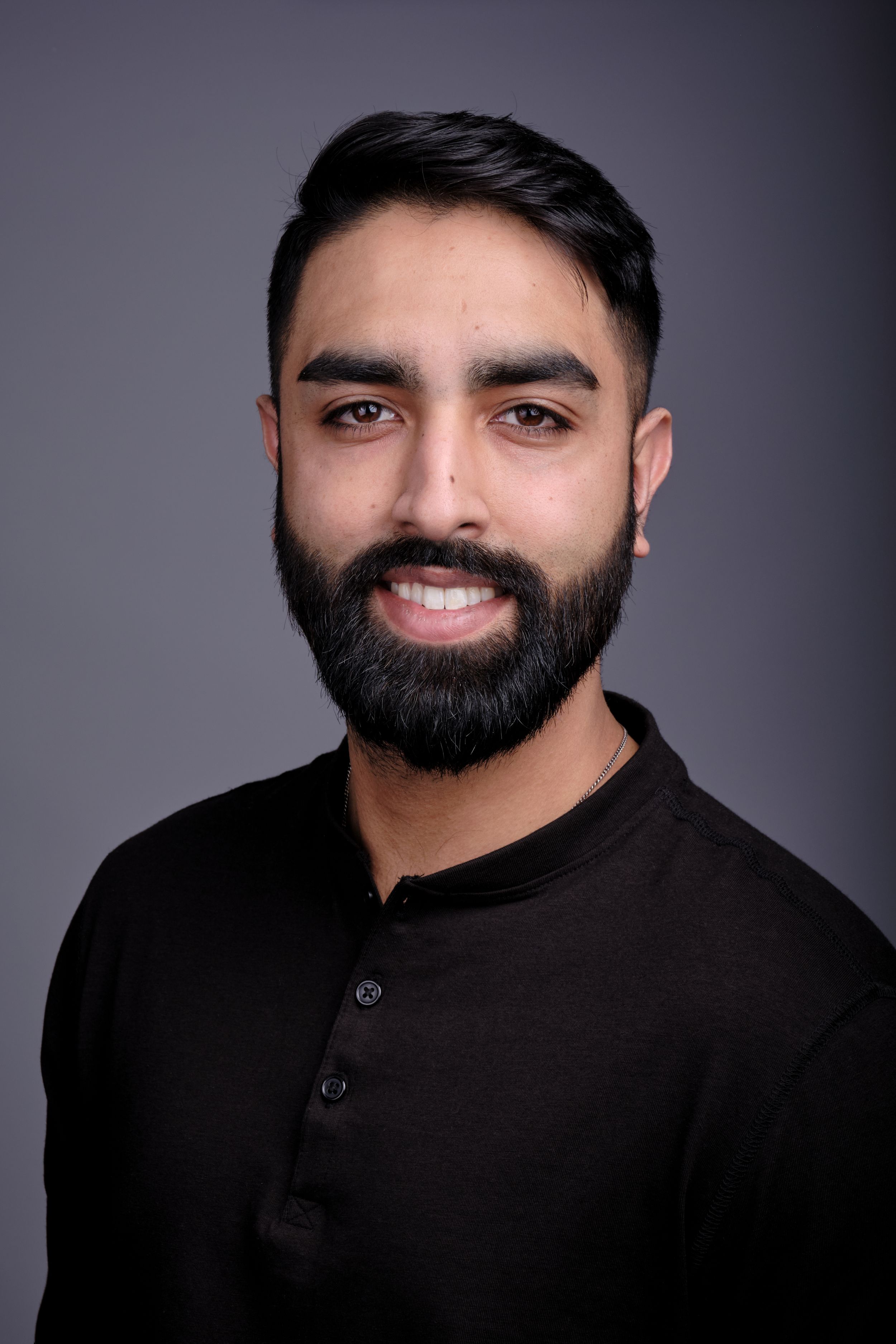 Studio portrait of person in black henley shirt against dark background.
